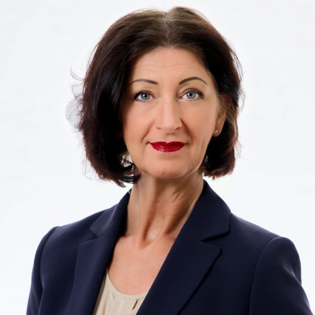 Carmen Lehner, professionelles Porträt im dunkelblauen Blazer vor hellem Hintergrund.