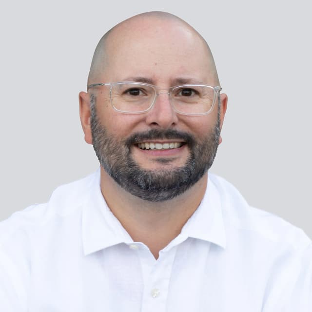 Dr. Jens Träger, lächelndes Porträt im weißen Hemd vor hellgrauem Hintergrund.